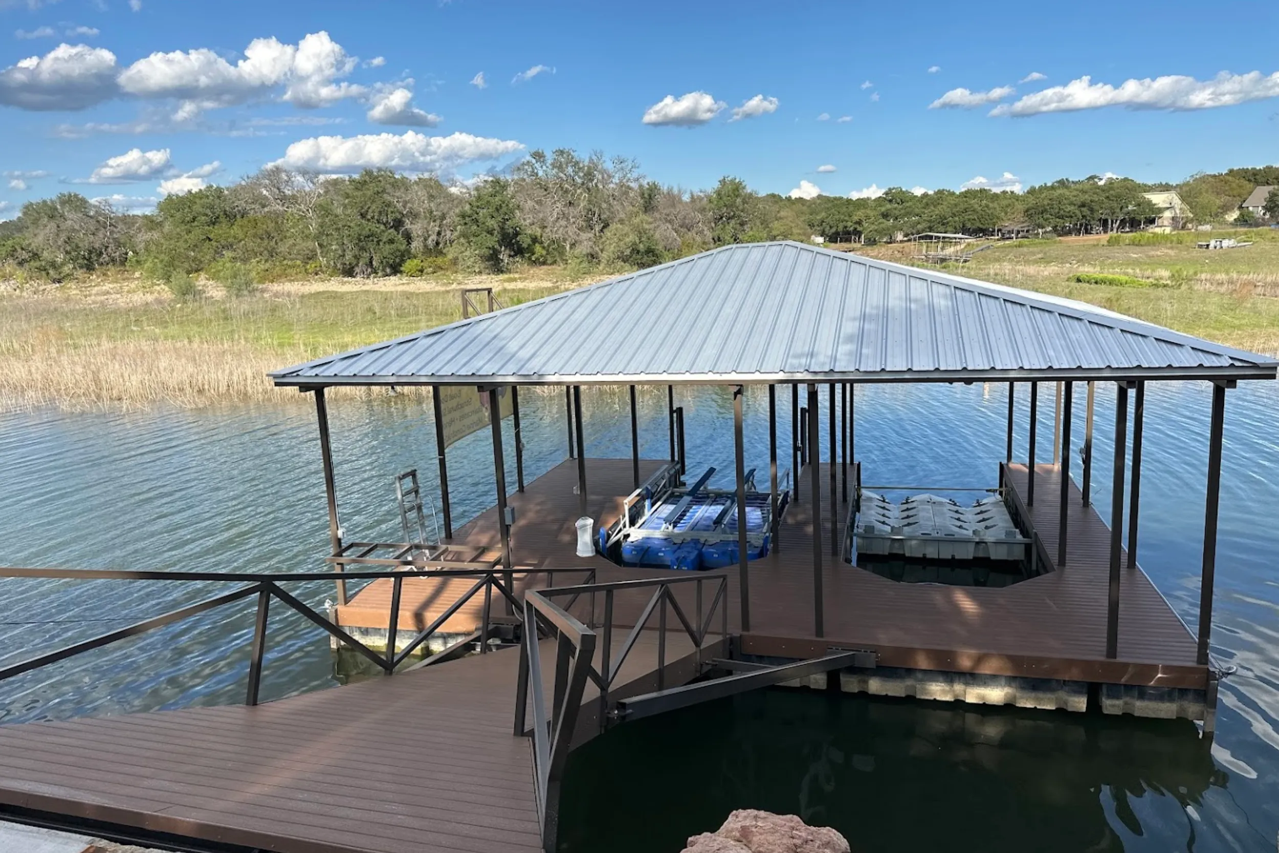 Covered floating dock with a wood deck, railing and boat slips on a Hill Country lake
