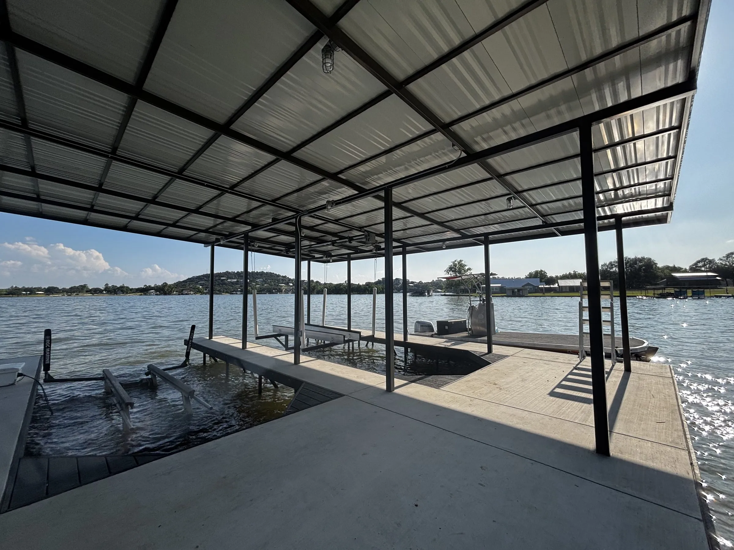 View from under the steel roof across the concrete deck and boat slip toward the lake