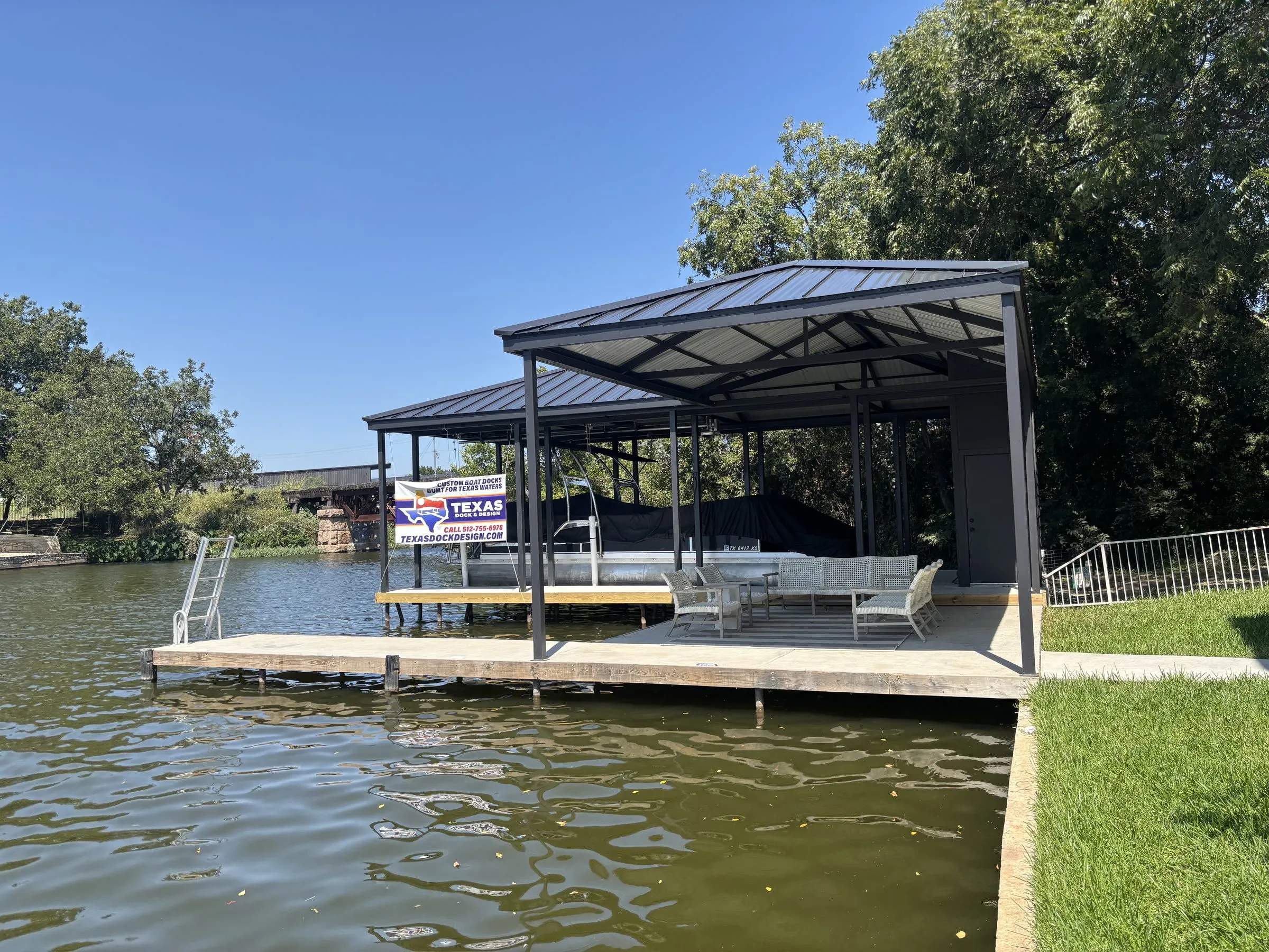 Stationary dock with a covered boat slip and patio seating, with a Texas Dock & Design banner