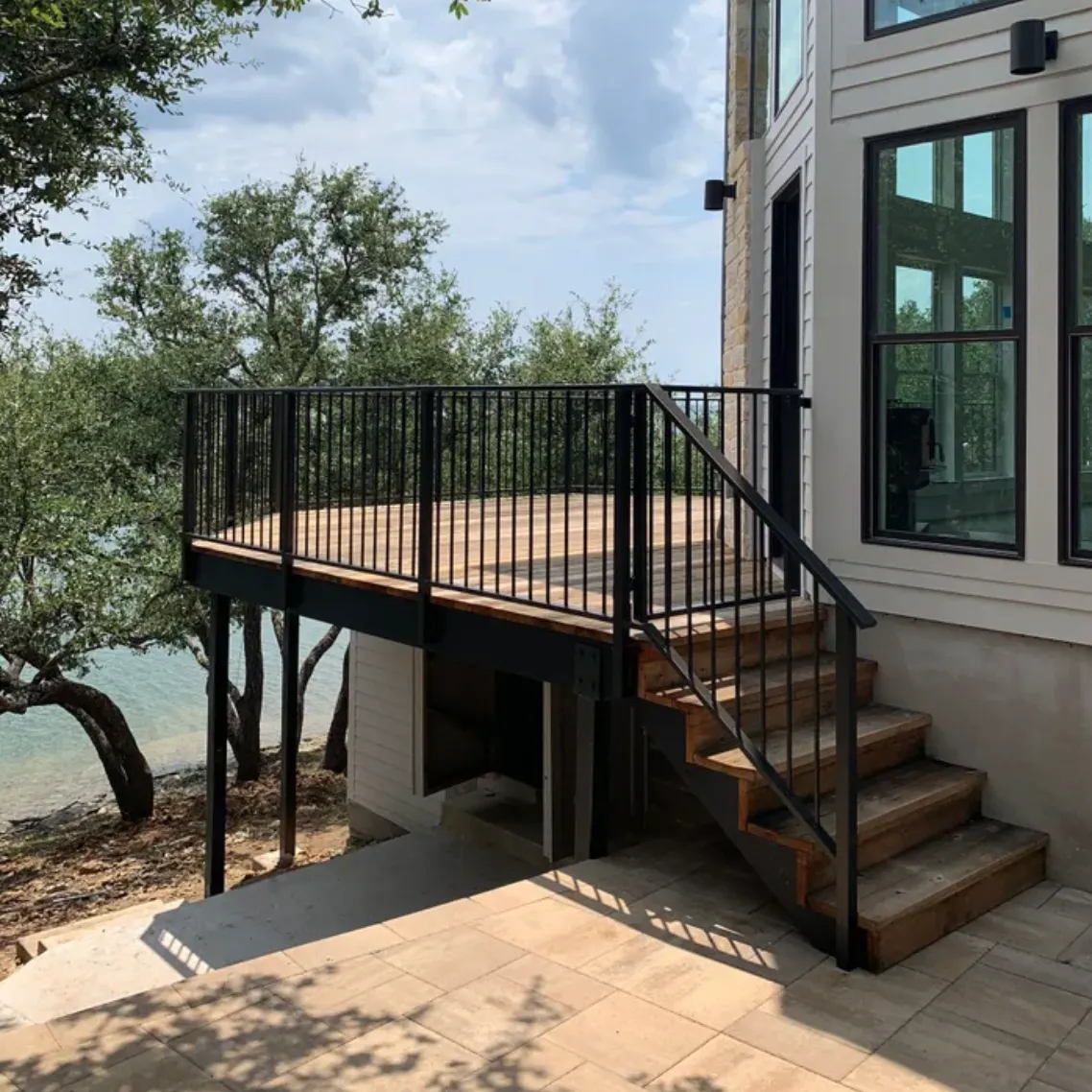 Elevated wood deck with steel stairs and black metal railing beside a lake house