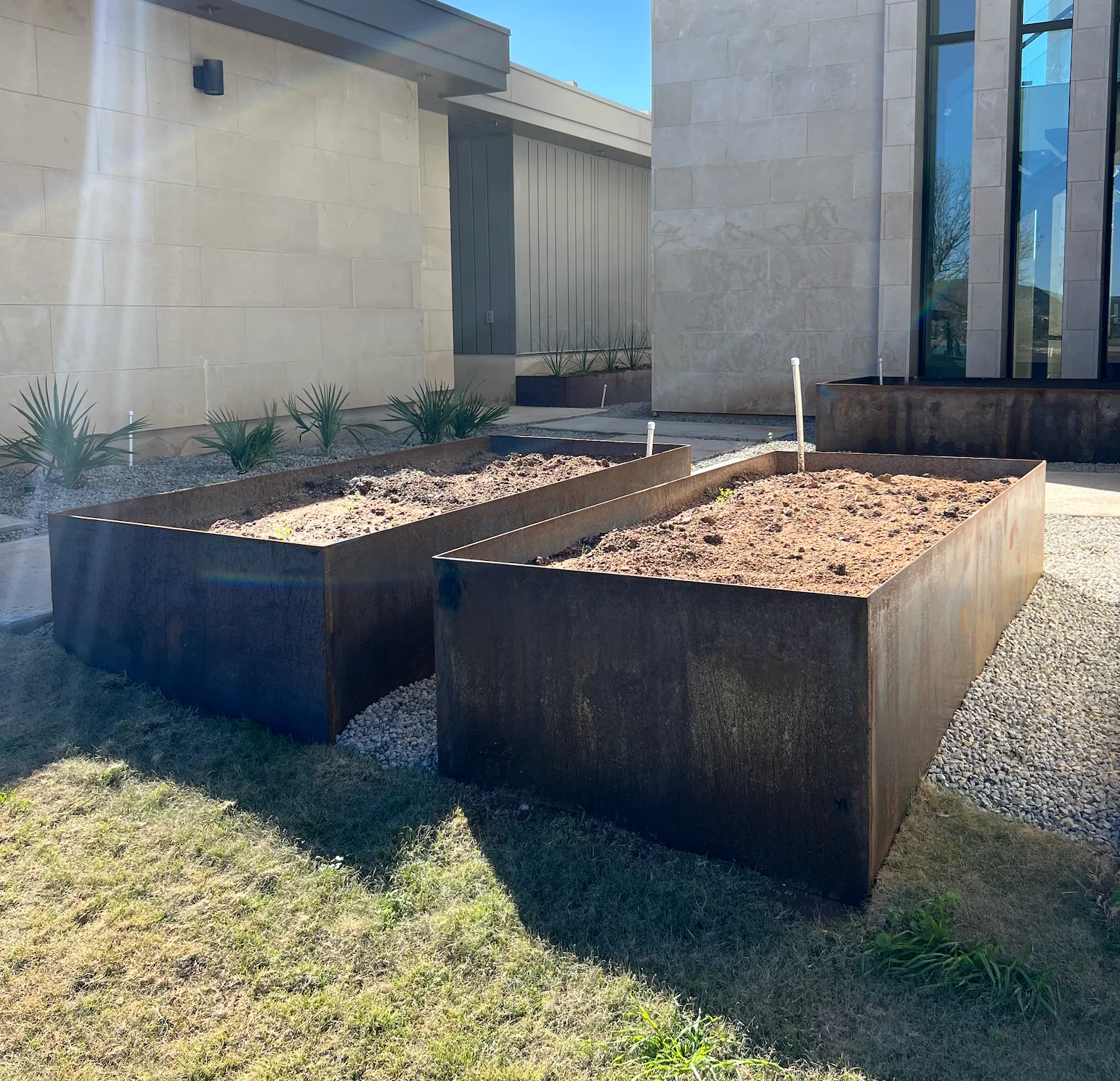Two large rectangular weathering-steel planter boxes beside a modern stone house