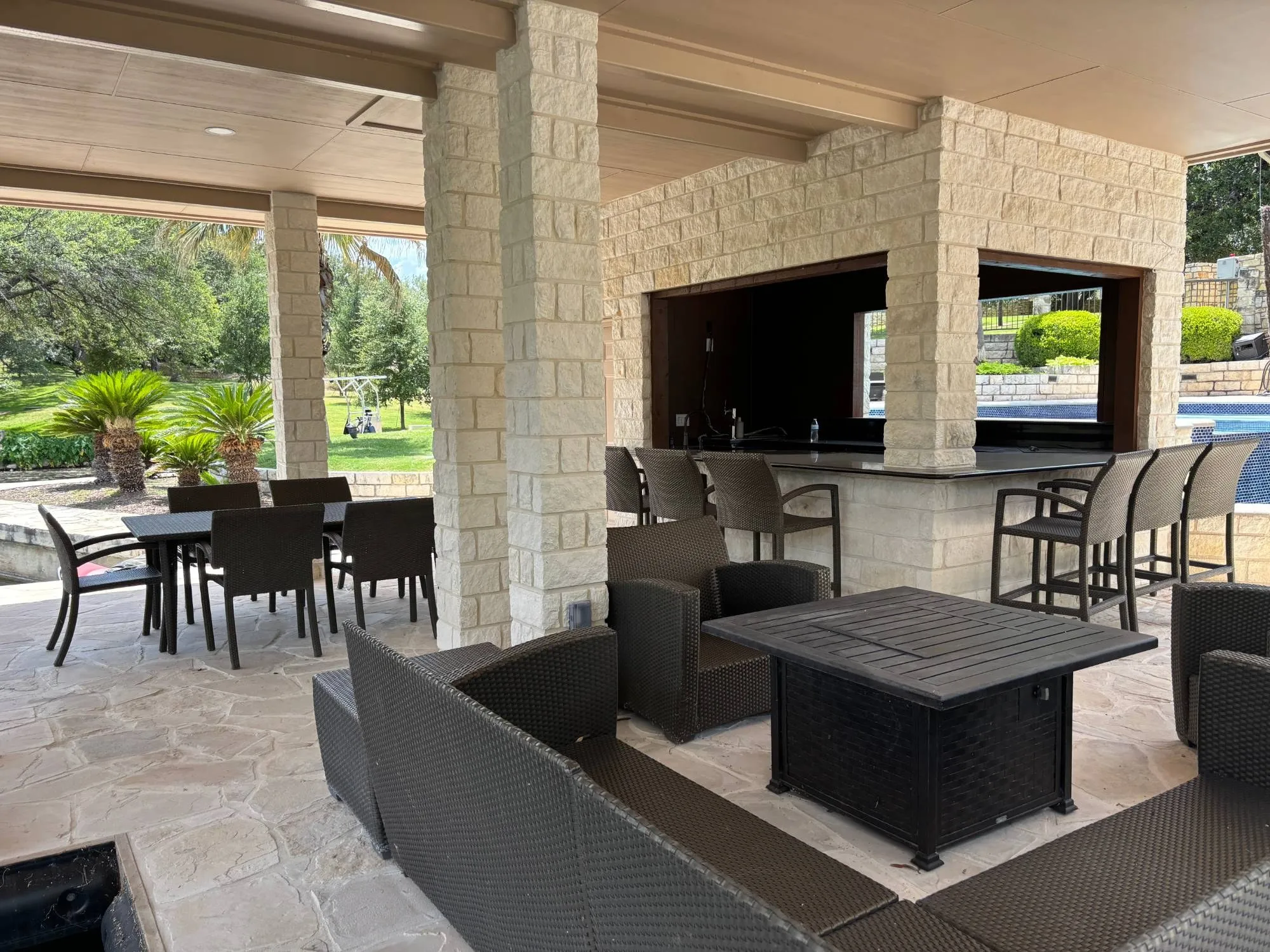 Lounge seating around a fire table under the pavilion roof, with a dining table and the stone bar behind